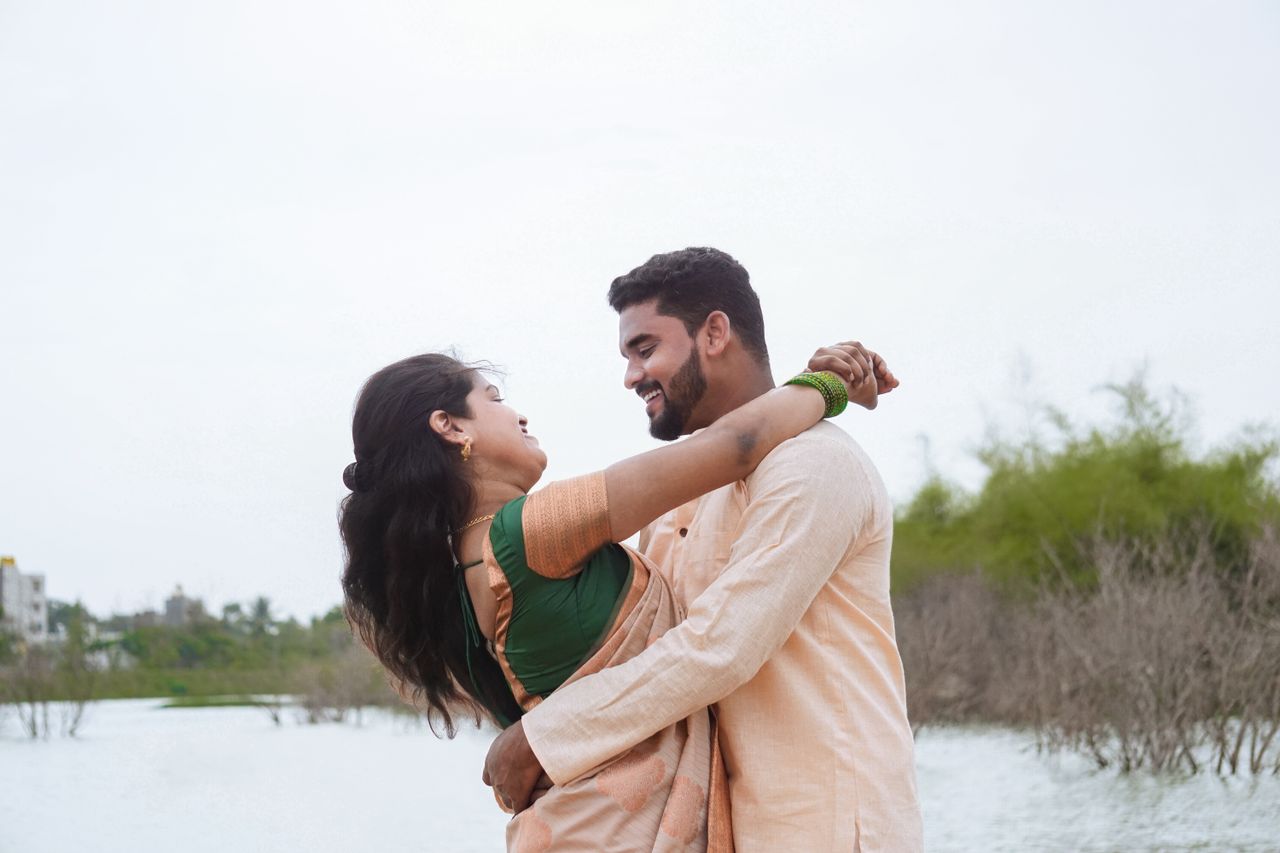 Indian couple joyfully embracing near a water body, exuding happiness and connection.