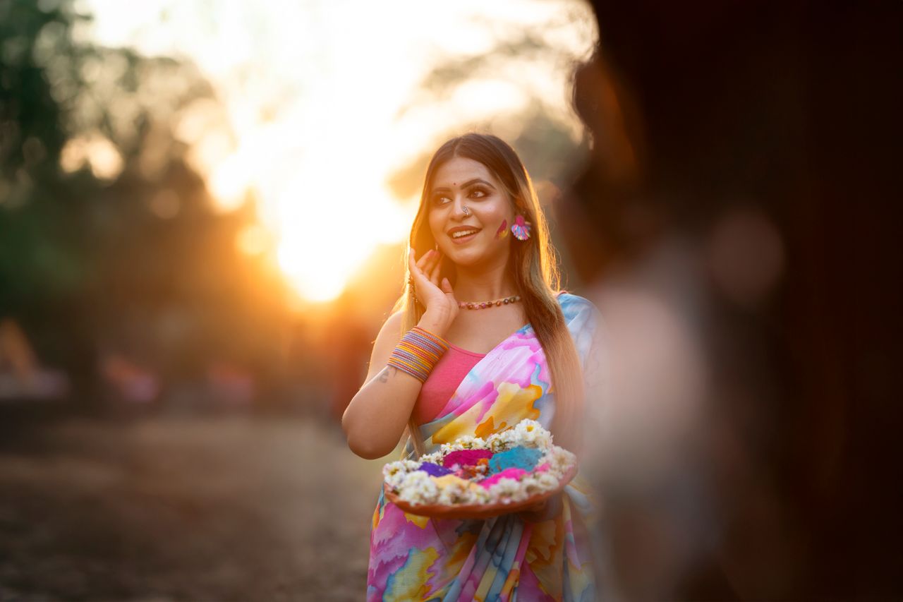 A woman joyfully celebrating Holi outdoors with vibrant colors and traditional attire at sunset.