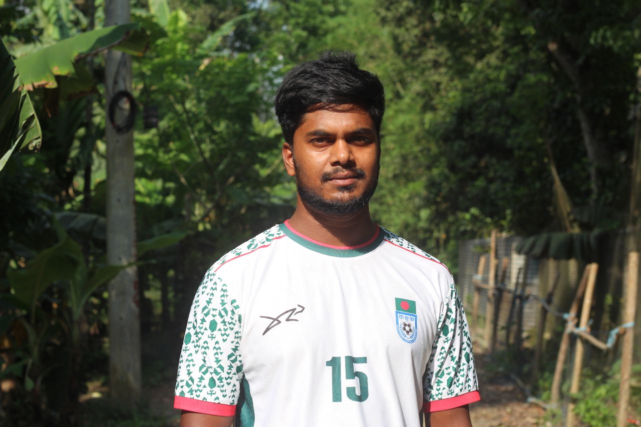 Young man standing outdoors in a sports jersey, surrounded by lush green foliage.