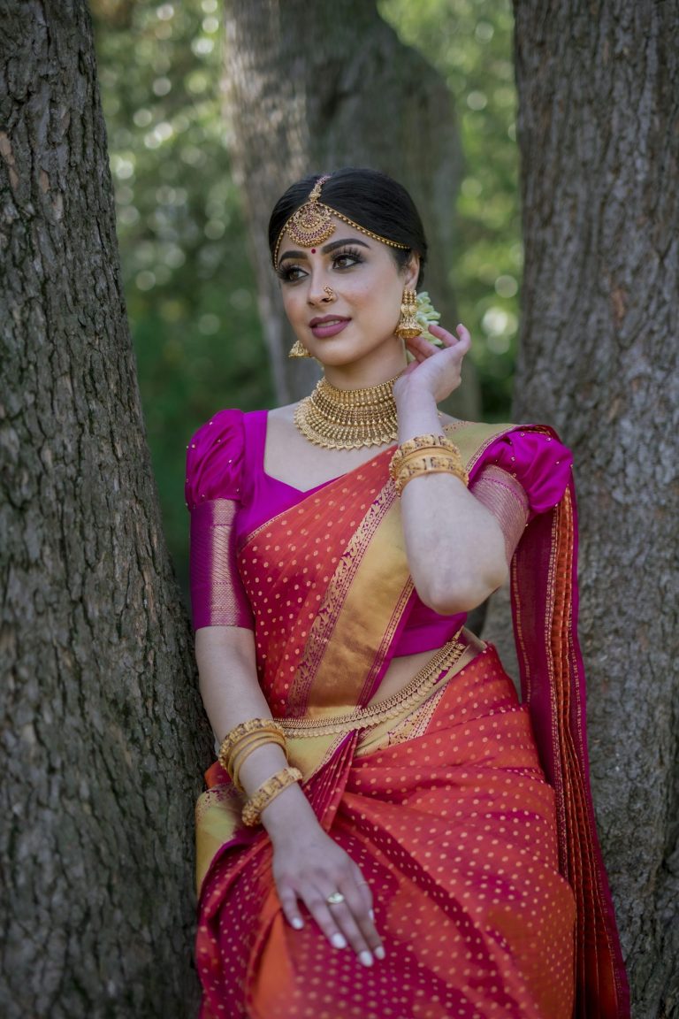 Woman in a pink and orange sari with gold jewellery between two trees